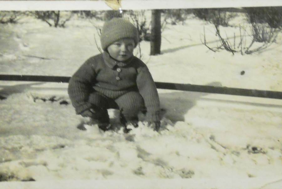 Czarno-biało zdjęcie małego chłopca bawiącego się na śniegu w parku.
