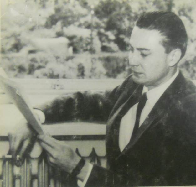 Czarno-białe zdjęcie młodego mężczyzny ubranego w garnitur, czytającego coś z notatnika.